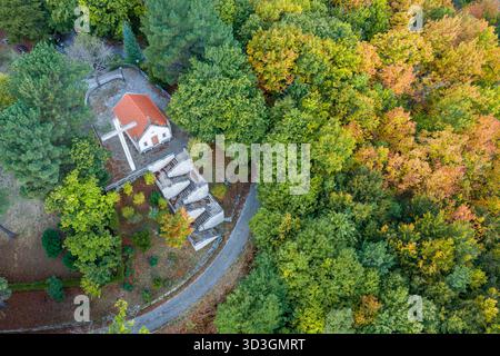 Blick aus der Vogelperspektive auf eine malerische Kapelle mit einem rot gekachelten Dach neben einer gewundenen Straße, umgeben von einem lebhaften Teppich aus Herbstlaub, Manteigas, Ser Stockfoto