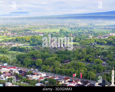 Blick aus der Vogelperspektive auf die antiken Tempel, die sich inmitten eines Meeres aus üppigen grünen Bäumen erheben, mit fernen Bergen, die den Horizont bemalen, Yogyakarta, Daerah Istimewa Yogya Stockfoto