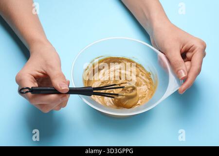 Frau mischt Haarfarbe in Schüssel auf hellblauem Hintergrund, Nahaufnahme Stockfoto