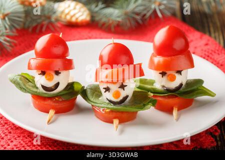 Köstliche Schneemänner aus Mozzarella, Tomaten und Basilikum auf Spießen in Nahaufnahme auf einem Teller auf dem Tisch. Horizontal Stockfoto