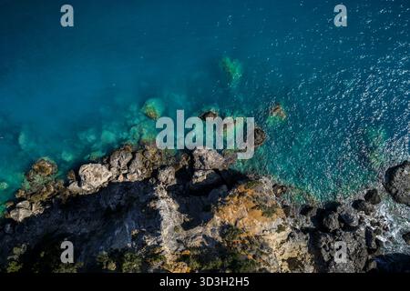 Aus der Vogelperspektive treffen auf das türkisfarbene Meer, wo die felsige Küste im Kontrast zum glitzernden Wasser steht, Himara, Albanien. Stockfoto