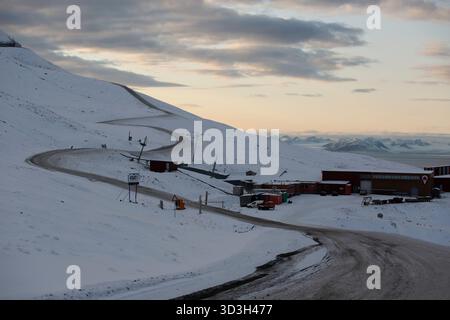 Longyerbeyen, Svalbard, Snowy Mountain mit einer Straße, die zu einem roten Gebäude führt. Die Straße ist mit Schnee bedeckt und das Gebäude ist von Schnee umgeben Stockfoto