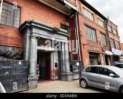 Manchester, Großbritannien - 30. September 2025: Industriebausteinfassade mit Steineingang, stapelbaren Reifen und einem geparkten Auto in Manchester. Stockfoto