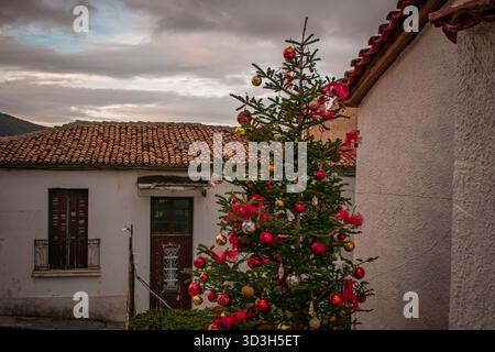 Weihnachtsbaum, der mit verschiedenen Kugeln, Lametta und Lichtern dekoriert ist, steht auf einer Stadtstraße von Delphi, Griechenland. Stockfoto