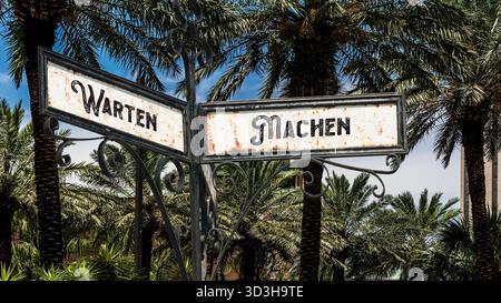 Ein Bild mit einem Wegweiser, der in zwei verschiedene Richtungen auf Deutsch zeigt. Eine Richtung ist zu tun, die andere zu warten. Stockfoto