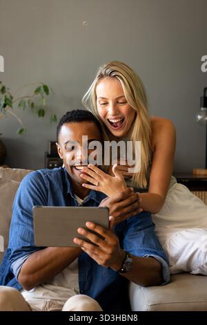 Paare sitzen auf der Couch und schauen sich ein Tablet an, um gemeinsam spannende Momente zu teilen. Zweisamkeit, Paare, Bindung, Technologie, Freizeit, Happiness || Model veröffentlicht Stockfoto