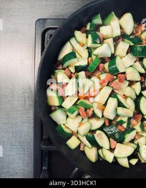 Gewürfelte Zucchini und Pancetta in einer schwarzen Pfanne auf dem Herd gebraten. Eine Zutat für eine Pasta oder eine Beilage. Italienisches Essen. Draufsicht. Stockfoto