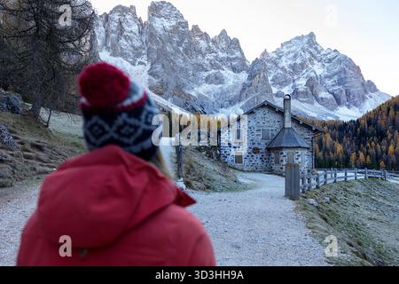 Tourist an einer hölzernen Berghütte in Val Venegia an einem Herbstmorgen, mit der atemberaubenden Dolomitenkette der Pale di San Martino im Hintergrund. Stockfoto