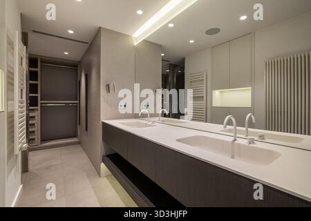 Modernes Bad mit zwei Waschbecken, eleganten Schränken und heller Beleuchtung. Minimalistisches Design mit neutralen Farben und geräumigem Layout. Stockfoto