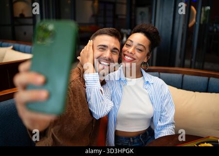 Ein vielseitiges Paar mit Feinschmecker genießt ein zwangloses Abendessen und einen Telefonmoment, bei dem sonnige Vibes und Drinks geteilt werden Stockfoto