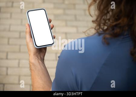 Athlet oder sportlich fitter Mann, der ein Mobiltelefon mit leerem weißen Bildschirm in der modernen Stadt hält. Mock-Up. Überprüfen Sie Apps, die sich auf das Gerät konzentrieren, chatten oder im Internet surfen. Im Freien. Stockfoto