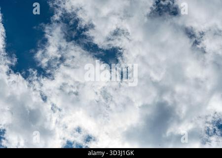 Kleines Flugzeug, das über den hellblauen Himmel mit weichen weißen Wolken fliegt. Minimalistische Szene, die Reisen, Freiheit und Erkundung symbolisiert. Stockfoto