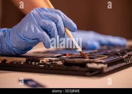 Techniker, der blaue Handschuhe trägt und einen Schraubendreher verwendet, um die internen Komponenten eines Laptops zu reparieren oder zu montieren. Nahaufnahme der Wartung der Computerhardware Stockfoto