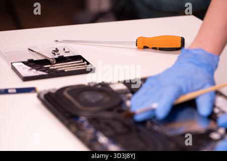 Techniker, der blaue Handschuhe trägt und einen Schraubendreher verwendet, um die internen Komponenten eines Laptops zu reparieren oder zu montieren. Nahaufnahme der Wartung der Computerhardware Stockfoto