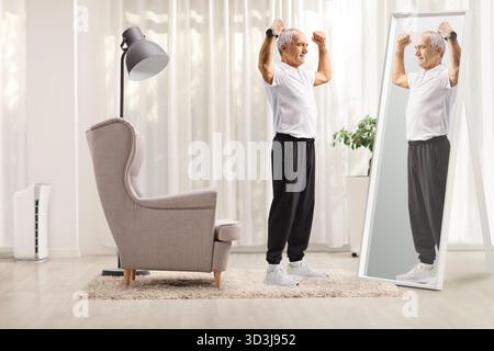 Älterer Mann in Sportbekleidung beugt Armmuskeln vor dem Spiegel zu Hause Stockfoto