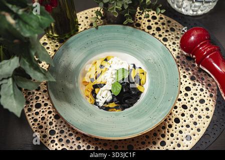 Essen, eleganter Teller mit schwarzer Tintenfischtinte und gelben Ei-Tagliatelle-Pasta mit cremiger Sauce und frischer Basilikumgarnitur, serviert in gehobenem Stil Stockfoto