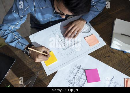 Projektentwurf. Dunkelhaariger junger Mann, der am Tisch sitzt und einen Projektentwurf vorbereitet Stockfoto