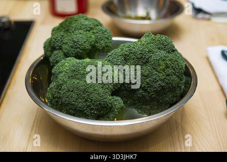 Lebensmittel, Nahaufnahme von leuchtend grünen Brokkoli-Röschen, die in einer Edelstahlschale auf einer hölzernen Küchenarbeitsfläche platziert werden und bereit zum Kochen oder Zubereiten sind Stockfoto