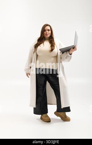 Eine junge Frau in Übergröße posiert selbstbewusst in einem gestrickten Winterpullover in einem hellen Studio. Stockfoto