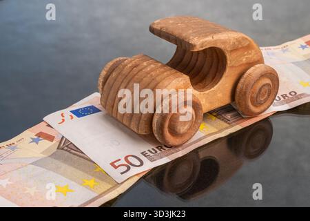 Ein Holzspielzeugauto fährt auf einem Stapel von 50-Euro-Banknoten, die Transportkosten und Finanzierungskosten darstellen. Stockfoto