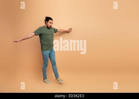 Junger Mann in lässigem grünem T-Shirt und Jeans posiert überraschend vor beigefarbenem Hintergrund Stockfoto