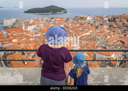 Weißen Mutter und Tochter Touristen wearnig blaue Hüte auf der alten Stadtmauer in Dubrovnik stehen mit Blick auf die historische Stadt unten Stockfoto