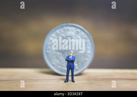 Miniaturmenschen : Geschäftsmann in der Nähe einer Münze mit hölzernem Hintergrund : Geschäftskonzept Stockfoto