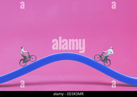 Miniaturreisende mit Fahrrad auf der Brücke auf rosa Hintergrund, Valentinstag-Konzept Stockfoto