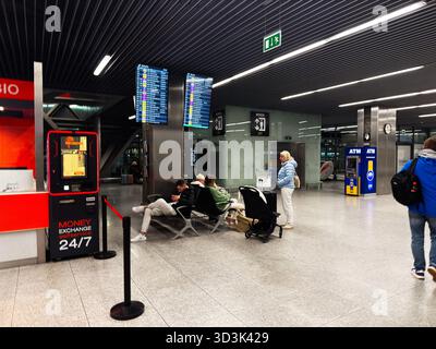 Balice, Polen - 4. Oktober 2025: Reisende warten in einem modernen Krakauer Flughafenterminal in der Nähe von Flugplattformen und Service-Desks. Stockfoto