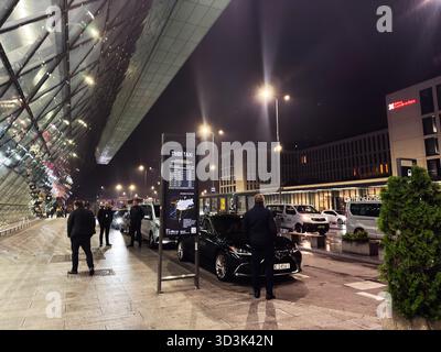 Balice, Polen - 4. Oktober 2025: Nachtszene vor dem Flughafen Krakau mit Taxis, Fahrzeugen und Passagieren neben einem modernen Glasterminal. Stockfoto