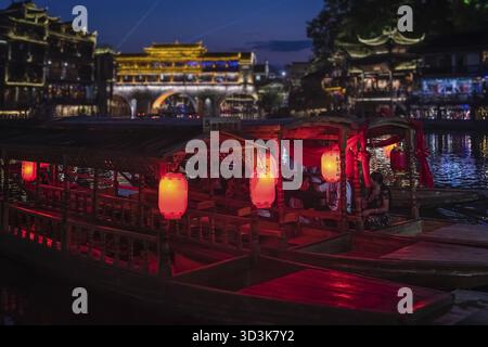 Feng Huang, China - August 2019: Rote, gelbe und orangene Laternen hängen an den alten historischen hölzernen Touristenbooten in der Altstadt von Feng huang Stockfoto