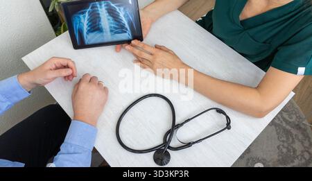 Aufnahme der Ärztin in Uniform mit Röntgenbild der Lunge auf der Tablette für den Patienten Stockfoto