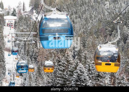 Ruzomberok, Slowakei - 4. Januar 2025: Farbenfrohe Gondeln der Skilifte, die sich während der Wintersaison über schneebedeckten Wald im Malino Brdo Resort bewegen Stockfoto