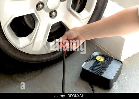 Nahaufnahme einer Frau, die Autoreifen mit einem tragbaren elektrischen Luftkompressor aufpumpt. Selbstgebaute Fahrzeugwartung zu Hause oder in der Garage. Stockfoto