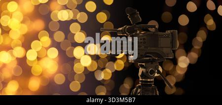 Videokamera gegen verschwommenes Licht auf dunklem Hintergrund, Bokeh-Effekt. Bannerdesign Stockfoto