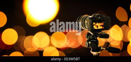 Professionelle Kamera gegen verschwommenes Licht auf dunklem Hintergrund, Bokeh-Effekt. Bannerdesign Stockfoto