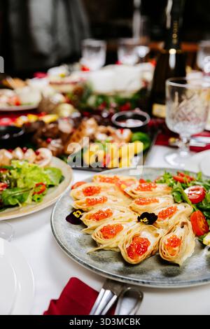 Festliche Krepprollen mit rotem Kaviar, Grün und Kirschtomaten auf elegantem Tisch Stockfoto