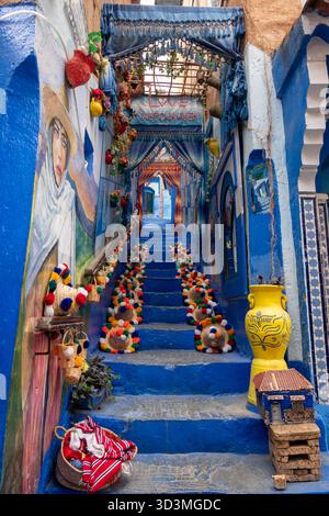 Chefchaouen, Marokko - 26. Oktober 2025: Hochdekorierte blaue Gasse in Chefchaouen mit lebendiger Straßenkunst, farbenfrohen Bommelmützen und einem Dekor Stockfoto