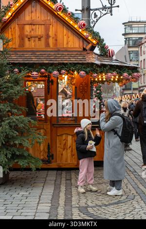 04.12.2024 Breslau, Polen. Traditionelles hölzernes Weihnachtsmarkt-Chalet mit rot gestreiften Ornamenten und warmen Lichtern, die Besucher genießen Stockfoto