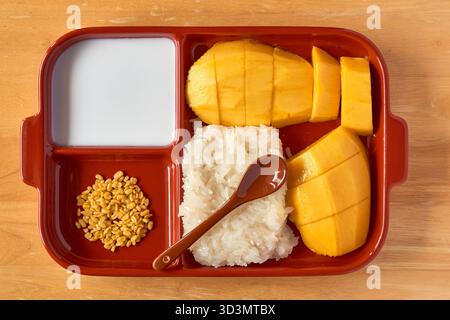Auf einem farbenfrohen Tablett befindet sich eine Portion Mangoreis mit Reifen Mangoblättern, garniert mit Kokosmilch und bestreut mit gerösteten Mungbohnen. Perfekt für Stockfoto