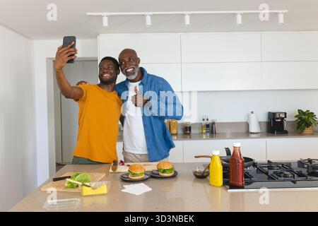 Afroamerikaner Vater und Sohn machen Selfie in der modernen Küche, mit Burgern und Smartphone Stockfoto