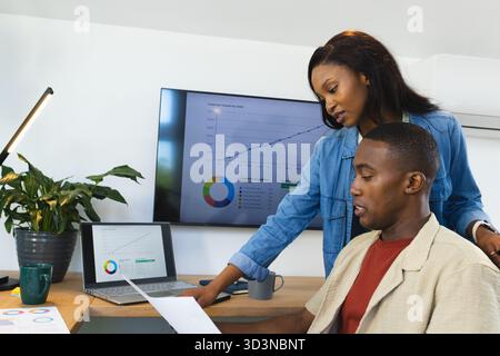 Afroamerikaner überprüfen den Bericht am Schreibtisch, Laptop zeigt Grafik, Kopierraum Stockfoto