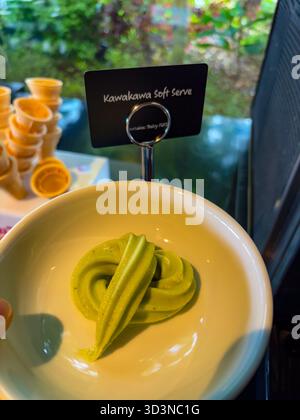 Kawakawa Softeis. Blassgrünes Wirbeln in einer weißen Schüssel an einer Selbstbedienungsstation mit Waffelkegeln im Hintergrund. Stockfoto