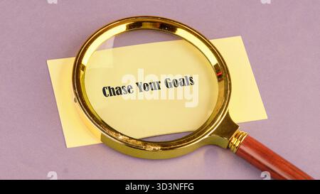 Eine Lupe hebt den Satz „Chase Your Goals“ auf einer gelben Note hervor und symbolisiert die Bedeutung von Klarheit und Entschlossenheit für das Erreichen von Perso Stockfoto