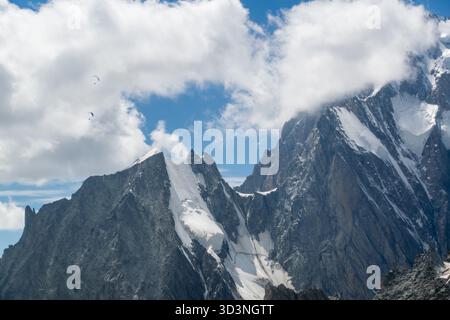 Abenteuer-Paragliding in der Nähe von zerklüfteten Gletscher-bedeckten Gipfeln am teilweise bewölkten alpinen Himmel Stockfoto