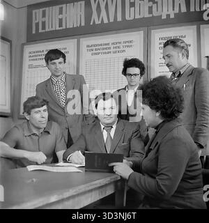 Ein Archivfoto aus dem Jahr 1981 zeigt ein Treffen in der AIZ (Armature-Isolator Plant) in Sloviansk, ukrainische SSR. Eine Gruppe von Ingenieuren und Arbeitern (fünf Männer und eine Frau) versammelt sich an einem Tisch zu einer Diskussion. Die Szene spielt unter einem großen Banner mit der Aufschrift „Beschlüsse des XXVI. Kongresses der KPdSU“, mit Plakaten über Produktionsquoten an der Wand dahinter. Dieses Bild fängt die Mischung aus industriellem Management und kommunistischer Parteiideologie in einer sowjetischen Fabrik ein. Dies ist ein Moment der täglichen Arbeit im friedlichen Donbass vor dem Krieg. Stockfoto