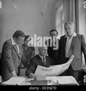 Ein Archivfoto aus dem Jahr 1981 zeigt eine Gruppe von Mitarbeitern der AIZ (Armature-Isolator Plant) in Sloviansk, ukrainische SSR. Fünf Kollegen (vier Männer und eine Frau) sind in einem Büro zu einem politischen Briefing versammelt. Ein leitender Angestellter, der an seinem Schreibtisch sitzt, liest einen artikel aus einer zentralsowjetischen Zeitung, wahrscheinlich "Prawda", während die anderen aufmerksam zuhören. Diese kollektive Lektüre der offiziellen Parteipresse war in der UdSSR eine gängige Praxis. Dies spiegelt die ideologische Seite des Arbeitsalltags im friedlichen Donbass vor dem Krieg wider. Stockfoto