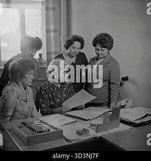 Ein Archivfoto aus dem Jahr 1981 zeigt ein Treffen des Frauenrates (Zhensovet) in der AIZ (Armature-Isolator Plant) in Sloviansk, Ukrainische SSR. Fünf weibliche Angestellte versammeln sich um einen Bürotisch, um zu diskutieren. Die sitzende Frau hält ein Dokument. Auf dem Schreibtisch befinden sich Ordner, ein Drehtelefon und ein traditioneller hölzerner Abacus (schoty). Diese Szene zeigt die administrative und soziale Organisationsarbeit in einer sowjetischen Fabrik. Dies zeigt den Alltag im friedlichen Donbass vor dem Krieg. Stockfoto