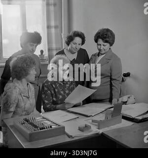 Ein Archivfoto aus dem Jahr 1981 zeigt ein Treffen des Frauenrates (Zhensovet) in der AIZ (Armature-Isolator Plant) in Sloviansk, Ukrainische SSR. Fünf weibliche Angestellte versammeln sich um einen Bürotisch, um zu diskutieren. Die sitzende Frau hält ein Dokument. Auf dem Schreibtisch befinden sich Ordner, ein Drehtelefon und ein traditioneller hölzerner Abacus (schoty). Diese Szene zeigt die administrative und soziale Organisationsarbeit in einer sowjetischen Fabrik. Dies zeigt den Alltag im friedlichen Donbass vor dem Krieg. Stockfoto