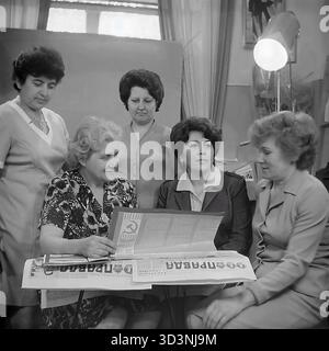 Ein Archivfoto aus dem Jahr 1981 zeigt ein Treffen des Frauenrates (Zhensovet) in der AIZ (Armature-Isolator Plant) in Sloviansk, Ukrainische SSR. Fünf weibliche Angestellte versammeln sich in einem Büro zu einer politischen Diskussion. Sie sitzen um einen Tisch, der mit Kopien der "Prawda", der offiziellen Zeitung der Kommunistischen Partei, bedeckt ist. Die Frauen lesen und diskutieren die Artikel. Diese Szene fängt die Mischung aus sozialer und ideologischer Arbeit innerhalb einer sowjetischen Fabrik ein. Dies zeigt den Alltag im friedlichen Donbass vor dem Krieg. Stockfoto